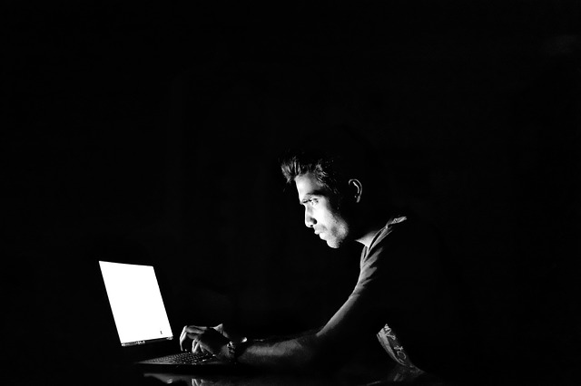 A working man in front of a laptop with the lights turn off