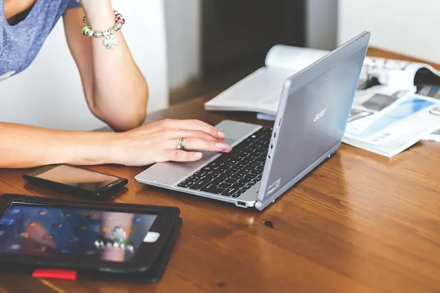 A woman using her laptop with a phone and a tablet beside her